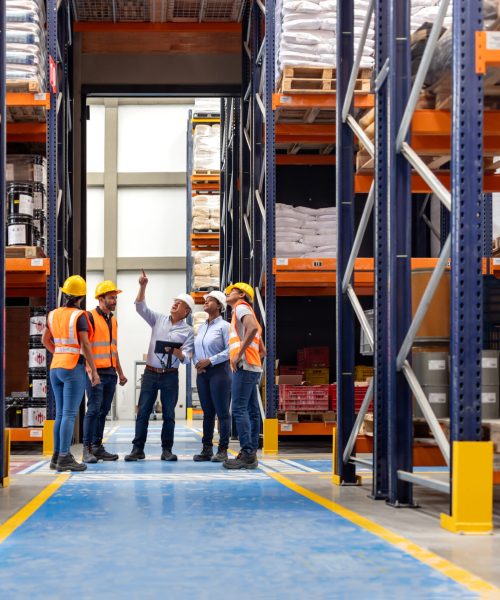 Forperson talking to a group of employees in a meeting at a distribution warehouse and pointing away